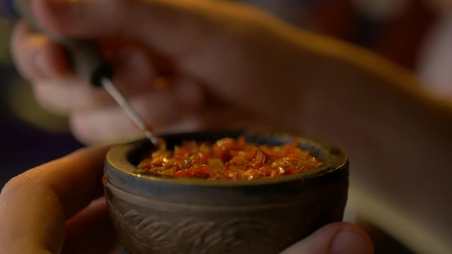 Preparing a bowl with tobacco for hookah. Worker hands with a needle straighten the workpiece. Close up.