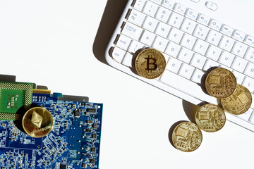 Gold coins with a bitcoin and ethereum symbol lying on white computer keyboard and graphic card. Concept of mining virtual crypto currency.