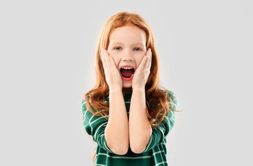 childhood, emotions and people concept - shocked or surprised red haired girl in green striped shirt screaming over grey background