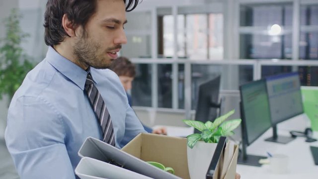 Sad Fired / Let Go Office Worker Packs His Belongings into Cardboard Box and Leaves Office. Workforce Reduction, Downsizing, Reorganization, Restructuring, Outsourcing. Mass Unemployment Market Crisis