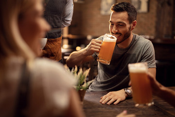 Young man drinking beer while being in a bar with his friends.