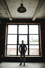 Silhouette of the guy in front of the window. Morning of the groom. Room in loft style. Big windows.