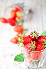 Organic red strawberries in two glasses and mint leaves on rustic wooden background.