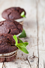 Chocolate dark muffins with mint leaves closeup on rustic wooden table.