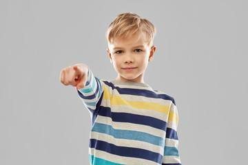 childhood, gesture and people concept - portrait of smiling little boy in striped pullover pointing finger over grey background