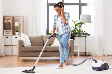 household, housework and cleaning concept - happy african american woman or housewife in headphones...