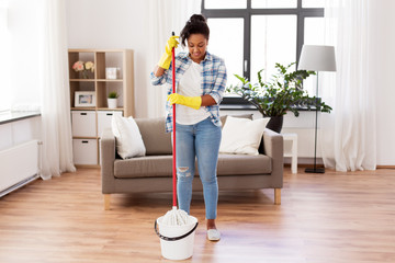 housework and housekeeping concept - african american woman or housewife soaking mop in bucket and cleaning floor at home