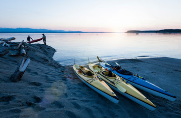 People men friends sea kayaking carrying boats on beach at sunset. Whidbey Island, Washington,...