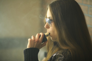 Obraz premium Vape teenager with problem skin. Portrait of young cute girl in sunglasses smoking an electronic cigarette in the bar. Bad habit that is harmful to health. Vaping activity.