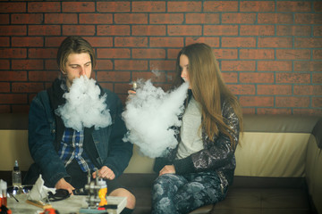 Vape teenagers. Young cute girl in sunglasses and young handsome guy smoke an electronic cigarettes in the vape bar. Bad habit that is harmful to health. Vaping activity.