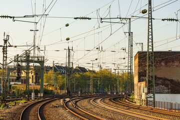Outdoor diminishing perspective view of curve railway track lines without train and mess complex electric cables and poles with golden light atmosphere and evening before sunset sky.