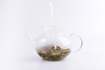Pouring hot water to the glass teapot with herbal tea, isolated on white background