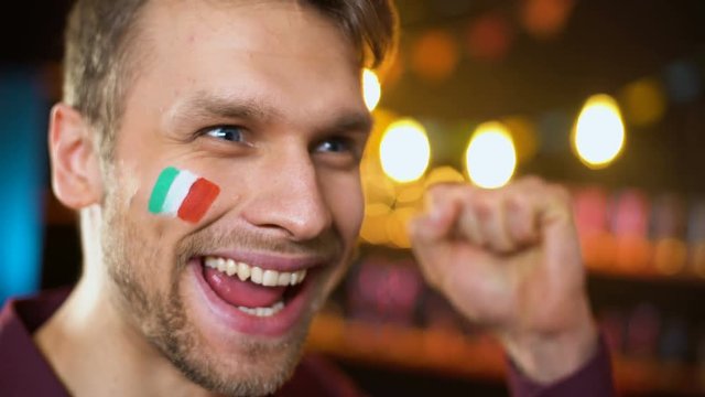 Cheerful italian fan with flag painted on cheek shouting, team scoring goal