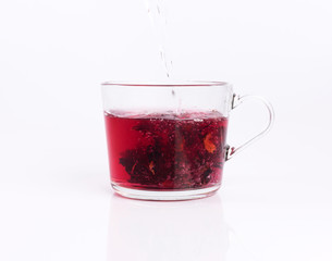 Pouring hot water to the glass cup with hibiscus tea, isolated on white background