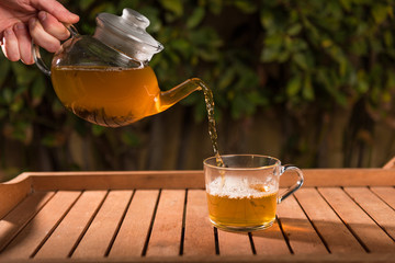 Pouring tea from teapot into a cup, natural background