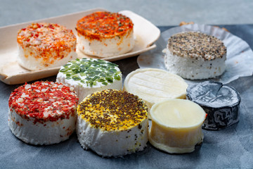 Assortment of French fresh white soft goat cheeses with different tastes topping made with herbs, paprika, indian curry, bruscetta, chives and dried tomatoes