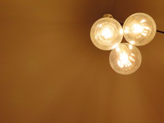 Three modern round lightbulbs close together, as a modern kind of lamp, illuminated with golden shining metal filament, seen from below, against rust color background, with copy space