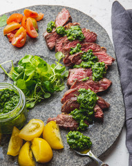 Slices of beef steak with chimmichuri sauce on gray stone plate