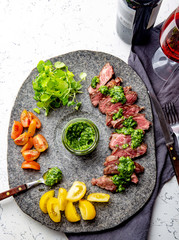 Slices of beef steak with chimmichuri sauce on gray stone plate