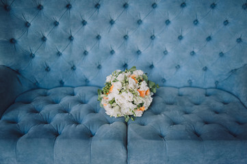 Multi-colored wedding bouquet with wildflowers and roses lies on the background of a blue sofa. Wedding photography, copy space, poster.