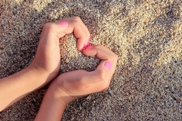 Girl hands forming heart shape in the sand on the beach. Summertime concept