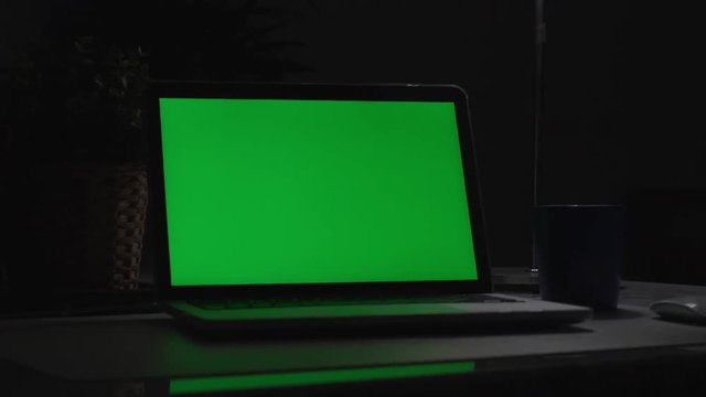 Laptop with green screen. Dark office. Dolly shoot. Perfect to put your own image or video.Green screen of technology being used. Chroma Key laptop