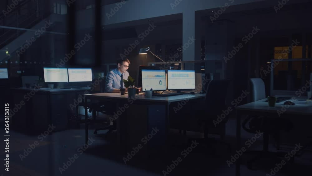 Poster working late at night in the office: businessman uses desktop computer, analyzing, using documents, 