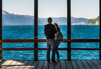 A couple in love on a travel standing on a wooden pier at the lake with blue water