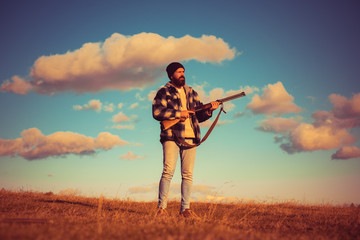 Bearded hunter man holding gun and walking in forest. Hunter with shotgun gun on hunt.