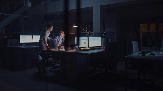 Ambitious and Confident Businessman Uses Desktop Computer, His Project Manager Explains Specific Tasks, Account Handling and Strategic Moves. Professional People Late at Night in Big Corporate Office