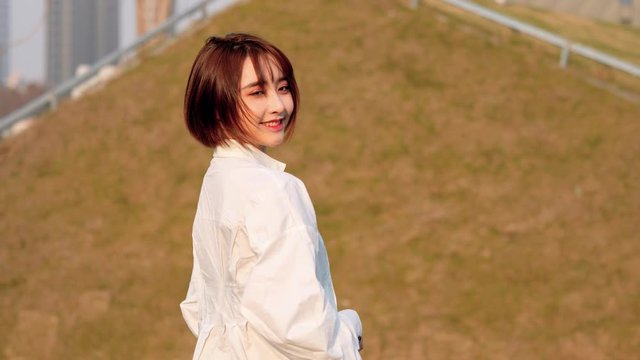 Beautiful Chinese girl in white shirt looking back and smiling at camera in windy and sunny day, sweet smile and cute blink, 4k movie, slow motion.