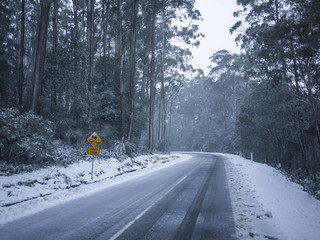 Slippery road warning sign for car drivers on side of a snow covered road. Icy scenic mountain...