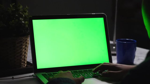 Over the shoulder shot of a young boy using on laptop computer on desk, looking at green screen. Dolly shoot 60fps.