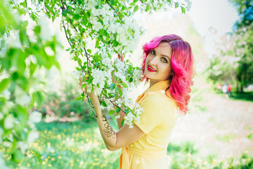 Beautiful and young woman with bright red hair and ref lips standing next to a blooming apple tree...