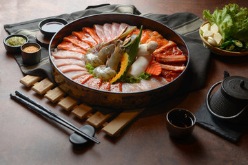 Side of beef garnished with sesame, and shellfish with prawns arranged on the tray combined with vegetables for grill set on the table.