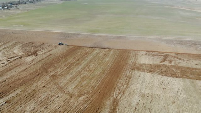 Aerial view blue tractor with four ploughshares cultivating dry fertile brown earth. The concept of agriculture. The magnificent scenery of the countryside