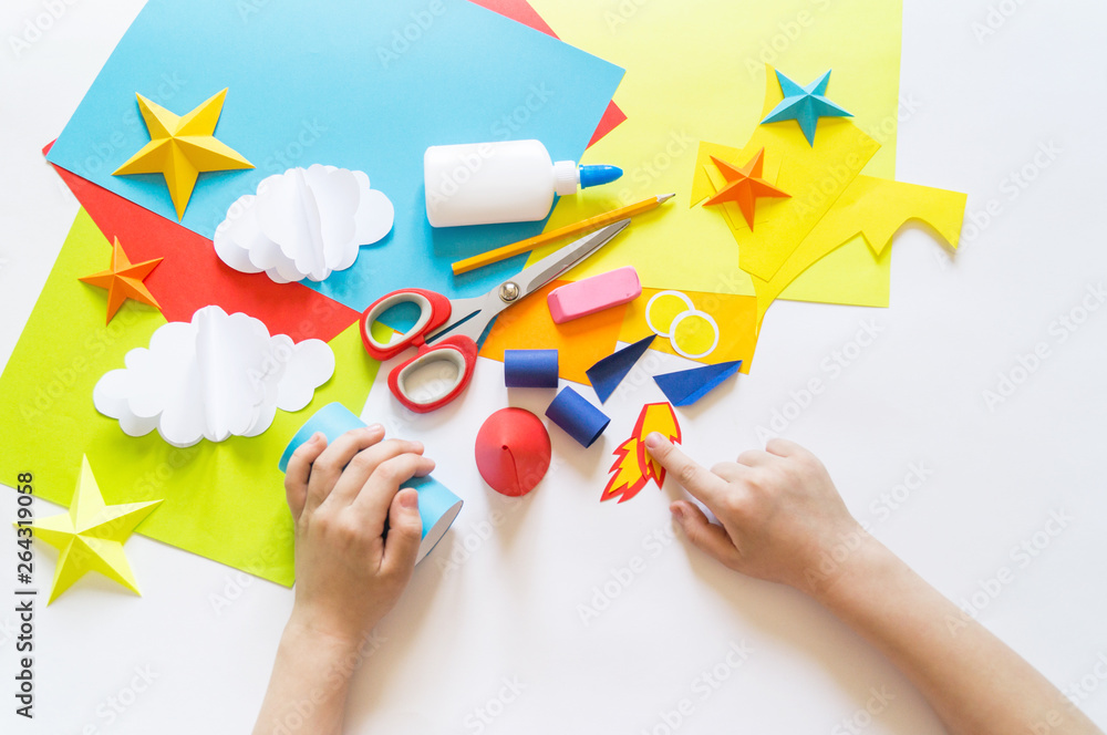 Wall mural hands of the child make a paper craft rocket. cosmos clouds and stars colored paper. the creative pr