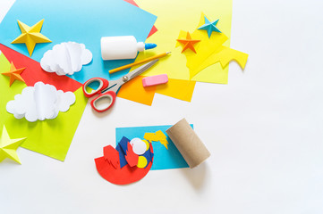 hands of the child make a paper craft rocket. Cosmos clouds and stars colored paper. The creative...