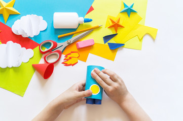 hands of the child make a paper craft rocket. Cosmos clouds and stars colored paper. The creative process