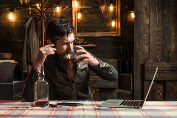 Fototapeta na wymiar Drinking man. Man with beard holds glass brandy. Man holding a glass of whisky. Sipping whiskey. Degustation, tasting. Macho is drinking whiskey by his laptop. Enjoy life.