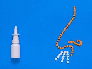 The nose of the tablets and spray for treating the common cold and allergies on a blue background. The concept of treatment of diseases of the nose and allergies. Flat lay.