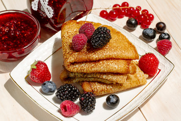 Pancakes with berries, Butter and tea in a white porcelain Cup. Healthy summer breakfast, homemade classic russian pancakes with fresh berry and sour cream, morning light white wooden background.