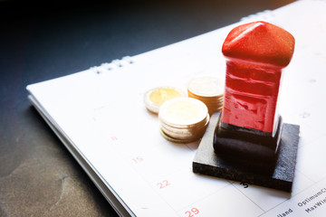 Close up red toy post box and money baht coin on the monthly planner calendar on black background. Summer calendar schedule. Calendar scheduling for travel,holiday and vacation planning or business co