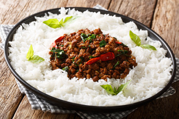 Thai recipe for basil chicken with chilli pepper and soy sauce with rice garnish close-up on a plate. horizontal