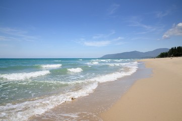 Fototapeta premium Turquoise tropical sea surf, wave foam, blue sky on empty sandy beach, Na Dan Beach in Khanom district of Nakhon Si Thammarat province of Thailand.