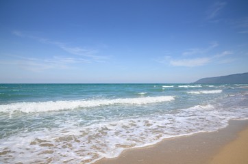Fototapeta na wymiar Turquoise tropical sea surf, wave foam, blue sky on empty sandy beach, Na Dan Beach in Khanom district of Nakhon Si Thammarat province of Thailand.