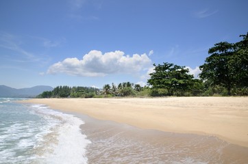 Turquoise tropical sea surf, wave foam, blue sky on empty sandy beach, Na Dan Beach in Khanom district of Nakhon Si Thammarat province of Thailand.