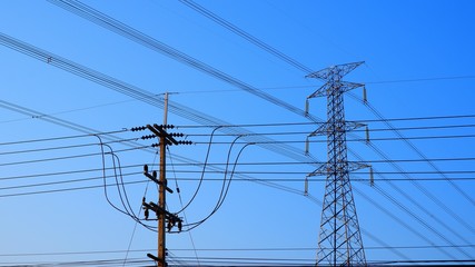 Electric pole with high voltage and many cable lines against blue clear sky background in sunny day, focus on foreground
