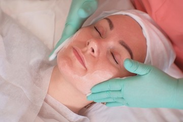 Naklejka premium The girl goes through facial treatments in the beauty salon. Beautician wearing gloves apply moisturizer on the woman's face. Facials at the Spa