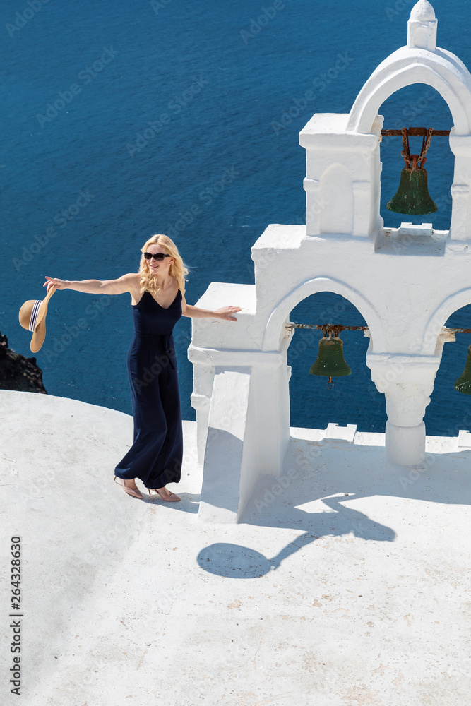 Wall mural blond woman next to a santorini bell tower in oia